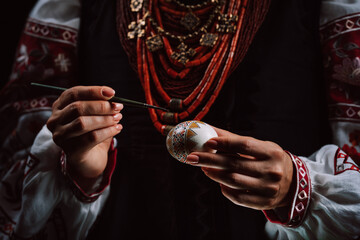 Ukrainian woman painting traditional ornamets on Easter egg - pysanka. 