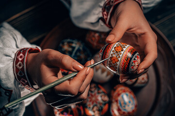 Ukrainian woman painting traditional ornamets on Easter egg - pysanka. 