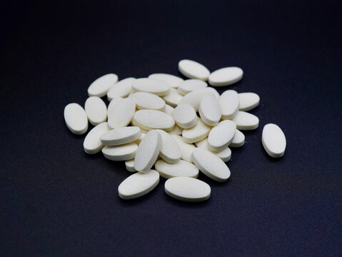 Flat lay of scattered vitamin B3 tablets on a plain dark backdrop. Modern and clinical aesthetic. Perfect for illustrating daily supplements or nutritional support themes