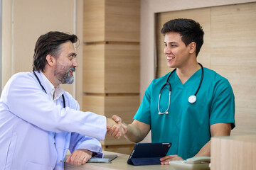 Senior doctor is handshaking with young nurse while having discussion on patient medical record after diagnosis for precise care plan with experienced physician specialist concept
