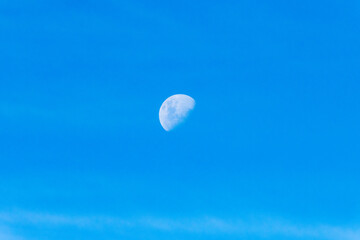 High cloud in the blue afternoon sky with a partial moon rising