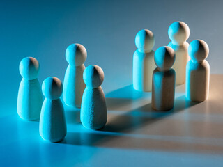 Wooden figures arranged in two separate groups under blue lighting, symbolizing division, teamwork,...