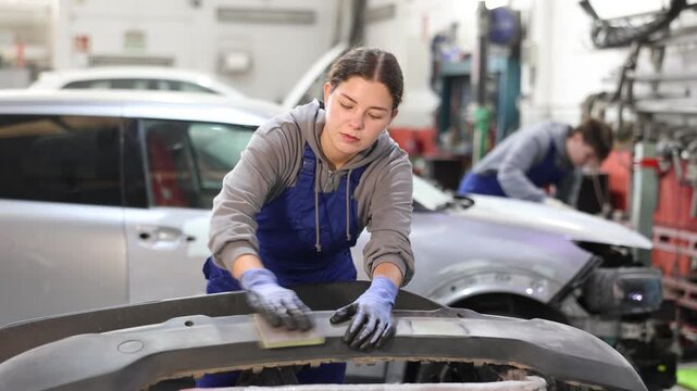 Girl car mechanic polishes car bumper - prepares bumper for painting in car service. High quality 4k footage