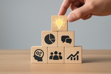 Hand placing lightbulb icon wooden block atop business concept blocks on wooden surface