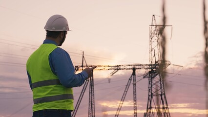 technology concept with high voltage power lines. electrical engineer helmet digital tablet sunset. power engineer power plant high voltage voltage energy. concept electrical engineer working sunset.