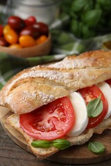 Tasty sandwich with mozzarella cheese, tomatoes and basil on wooden table, closeup
