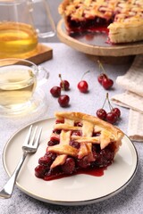Piece of tasty cherry pie, berries and tea on grey textured table, closeup
