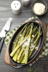 Tasty cooked asparagus served with parmesan on black wooden table, flat lay