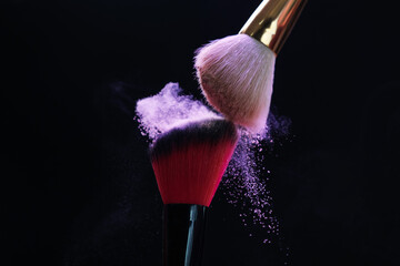 Makeup brushes with purple eye shadow on black background, closeup