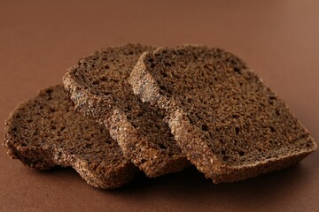 Pieces of fresh rye bread on brown background, closeup