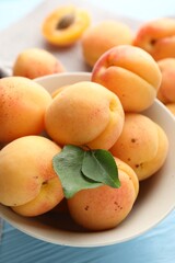 Fresh apricots with green leaves on light blue wooden table, closeup