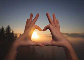 Hope. Woman making heart with hands against sun in mountains, closeup