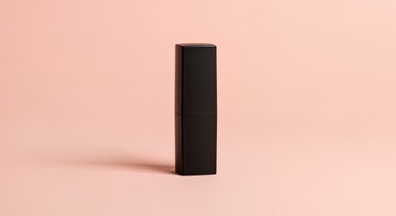 A sleek black cosmetic tube stands upright against a soft pink backdrop, showcasing its minimalist design and elegant simplicity.