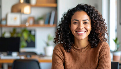 Portrait of a young Hispanic woman smiling naturally, sitting in a cozy modern home office, natural daylight