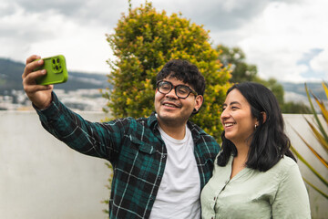 Latin american couple taking a selfie outdoors with smartphone