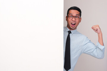 An Asian employee peeking behind wall showing his arms muscle with excited expression