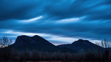 Obraz premium Mountain Silhouette Against Deep Blue Twilight Sky, Dusk Natural Landscape, Cool Ambient Light Creating Peaceful Wilderness Atmosphere for Outdoor and Nature Themes