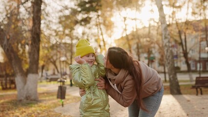 Fototapeta premium mother hugs child bright sunny park. childish smile. mother little happiness. warm day park. maternal love kid daughter. have fun together with parent autumn park yellow leaves. teamwork. laughter kid