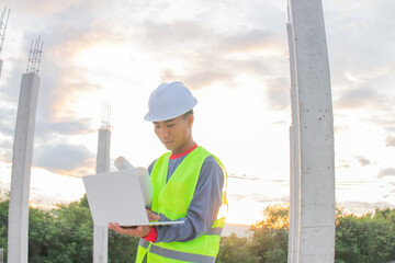 Young Asian construction professionals wearing hard hats are examining plans on site. They smile,...