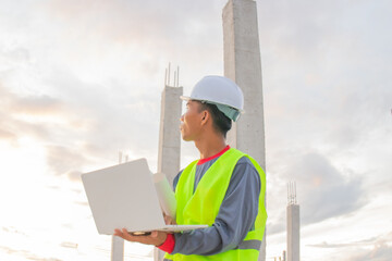 Young Asian construction professionals wearing hard hats are examining plans on site. They smile,...