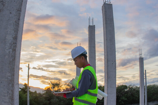Confident young male engineer wearing hard hat, checking checklist and blueprints at construction site, leading project planning with expertise, safety and professionalism.