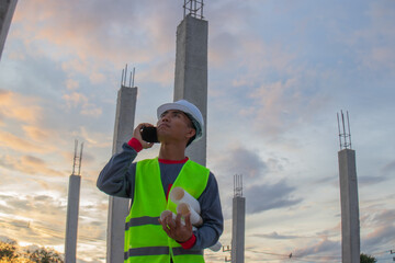 Confident young male engineer wearing hard hat, checking checklist and blueprints at construction...