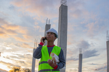 Confident young male engineer wearing hard hat, checking checklist and blueprints at construction...