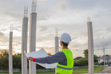 Confident young male engineer wearing hard hat, checking checklist and blueprints at construction...