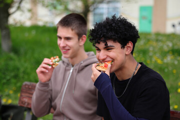 Fototapeta premium Two young guys eating pizza outdoor, picnic in park, dining outdoors