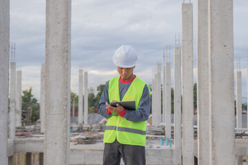 Confident young male engineer wearing hard hat, checking checklist and blueprints at construction...