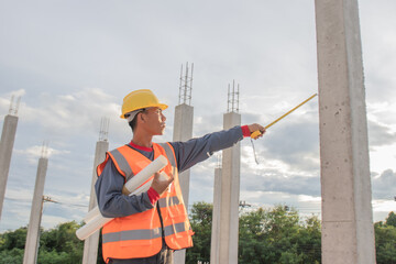 Male engineer in hard hat and safety vest examines blueprint indoors at construction site; planning infrastructure project with expertise, teamwork, and efficiency.