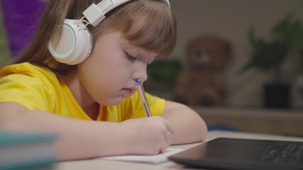 little schoolboy student writes mathematics notebook. child kid solves difficult learning problems. child education program. girl headphones with digital laptop writes notebook. study work home desk - Powered by Adobe