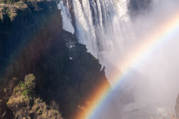 Telephoto shot of a rainbow being cast in front of the water thundering down victoria falls, in...