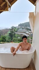 Handsome Man Relaxing in a Bubble Bath with Stunning Mountain View Amid Gentle Rain