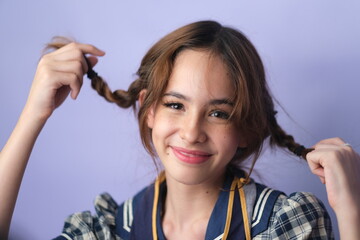 portrait of pretty young teenage girl with brown pony tails hair posing on violet. background.
