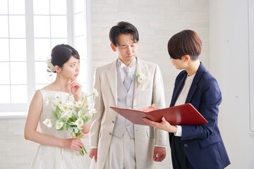 悩みながら打ち合わせする結婚式の司会者と新郎新婦