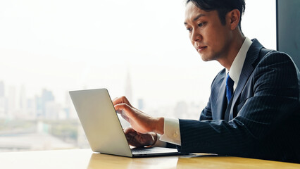 都市のオフィスビルでノートパソコンを使う男性ビジネスパーソン