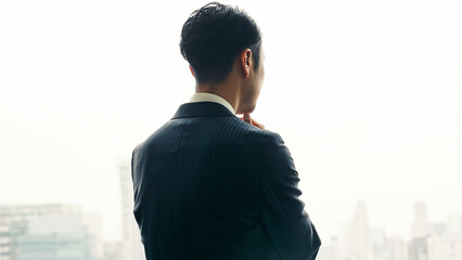 A male business person worries while looking at the city from the office window