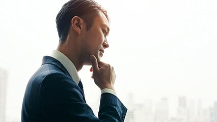 A male business person worries while looking at the city from the office window