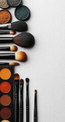 Makeup tools on white assorted eyeshadows and a range of brushes lie in a vertical line on the left of the frame, set against a textured white background