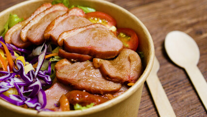 Sliced smoked duck breast nestled on crisp lettuce, vibrant tomatoes, purple cabbage, corn, and carrots in lightweight takeout container, presenting nutritious quick dining