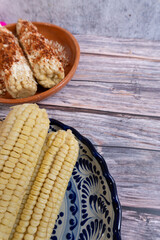 Top view of a table with cooked corn on the cob in the background, some already prepared corn on the cob, Mexican food