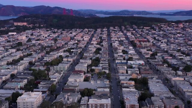 Aerial view of San Francisco, USA, at dusk. The Golden Gate Bridge is visible in the background. Rows of houses and streets fill the foreground.