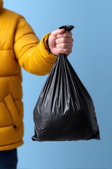 Taking out the trash, A person in a yellow jacket holds a full black garbage bag against a blue background.