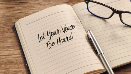 Opened notebook on a wooden desk with a pen and glasses, featuring the handwritten motivational...