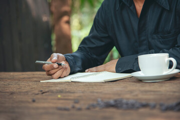 Man hands writing notebook diary with coffee cup and smartphone on wood desk. Close up man hands...