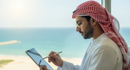 A businessman in traditional Middle Eastern attire uses a tablet and stylus while overlooking a stunning ocean view.