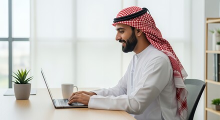 A smiling man in traditional Middle Eastern attire works on his laptop in a bright, modern setting.