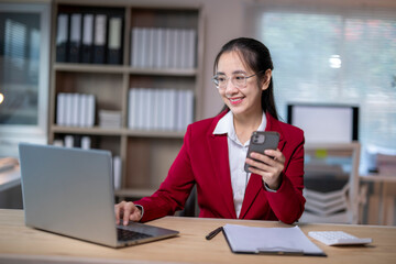 Fototapeta premium woman in a red jacket is sitting at a desk with a laptop and a cell phone