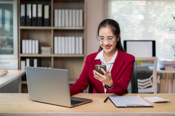 Fototapeta premium woman in a red jacket is sitting at a desk with a laptop and a cell phone